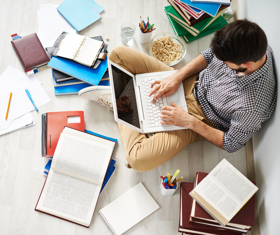 Man sitting on floor surrounded by books, on computer researching