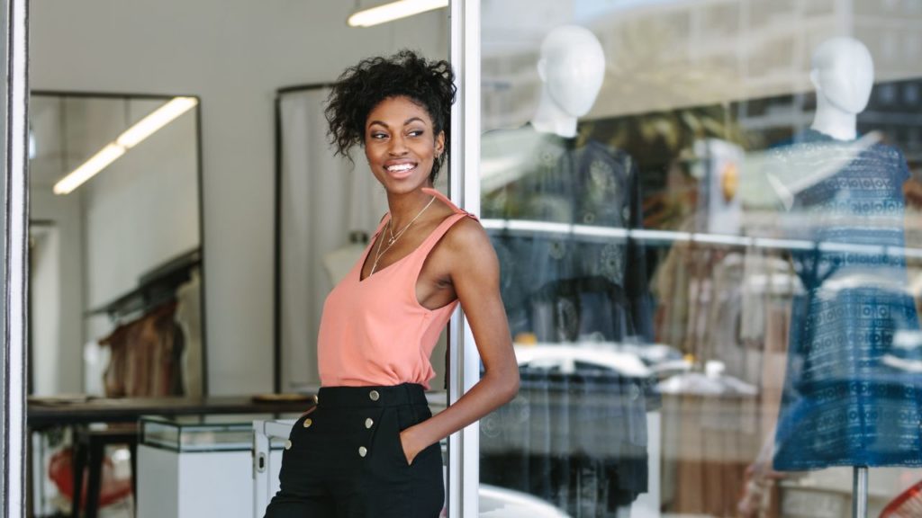 Woman standing in doorway of clothing store smiling with hands in pocket