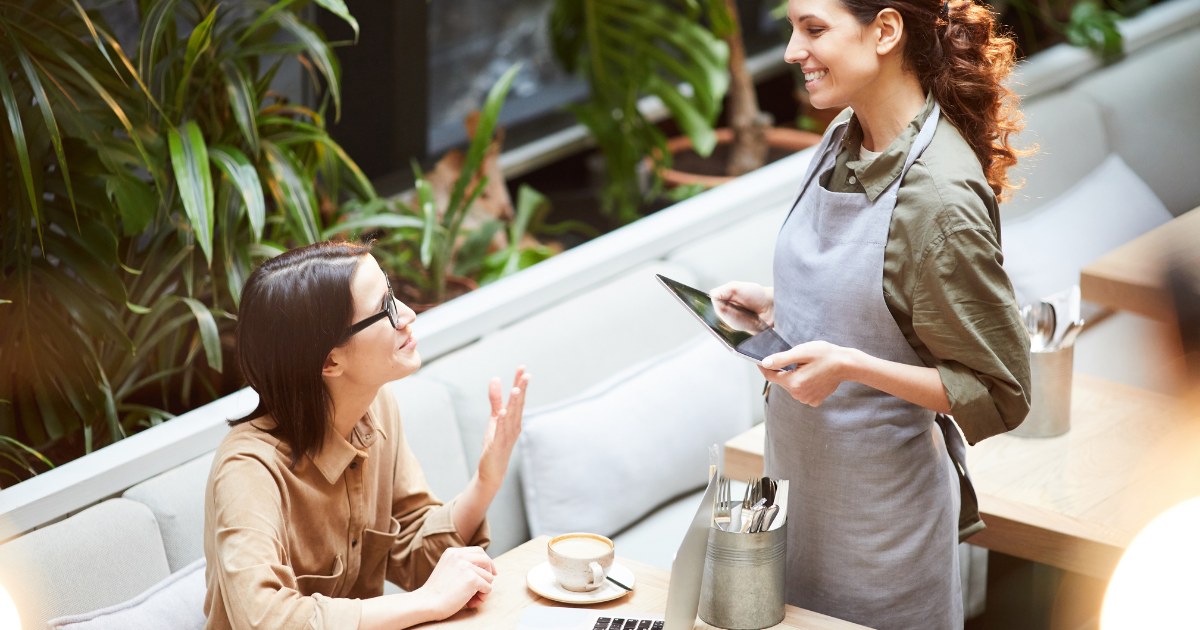 Woman at restaurant giving order to smiling waitress holding an ipad